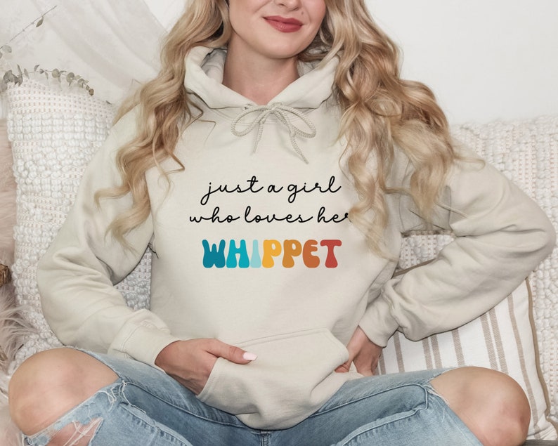 Może przedstawiać: Jasnobeżowa bluza z kapturem z napisem "just a girl who loves her WHIPPET" w kolorowej czcionce retro.