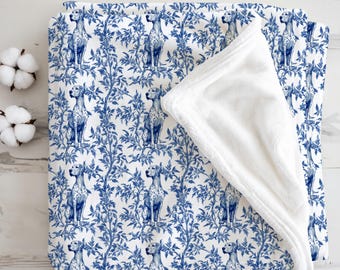 May include: A white and blue blanket with a repeating pattern of dogs and foliage. The dogs are depicted in a seated position. The blanket has a soft, white, plush underside. The design has a classic, decorative aesthetic.