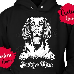 Peut inclure: Sweat-shirt noir avec une illustration blanche d'un chien teckel. Le texte "Buddy's Mom" est situé sous le chien. Deux éclaboussures de peinture rouge sont visibles sur le sweat-shirt, l'une dit "Custom Name" et l'autre "Custom Quote".