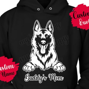 Puede incluir: Sudadera con capucha negra con un gráfico de perro pastor alemán blanco y el texto "Buddy's Mom". Hay un cuadro de texto rojo y blanco que dice "Custom Name" en la manga izquierda y un cuadro de texto rojo que dice "Custom Quote" en la manga derecha.