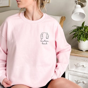 May include: A pink sweatshirt with a black outline of a dog's head and the text "Custom text" on the front.