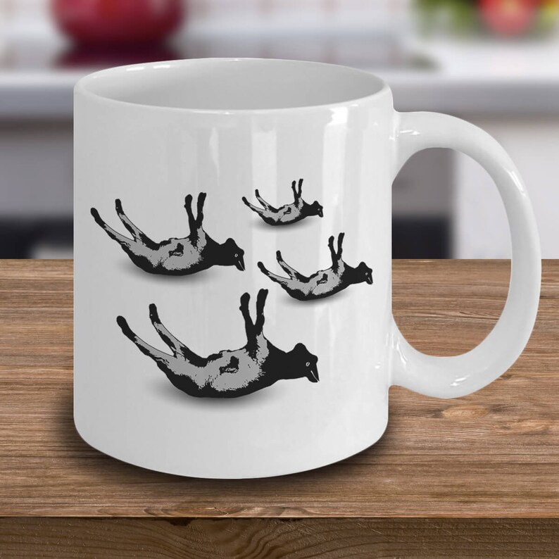 May include: White ceramic coffee mug with a black and white graphic of four sheep falling from the sky. The sheep are in different positions, with their legs and heads pointing in various directions.