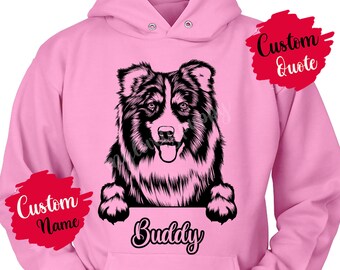Puede incluir: Sudadera rosa con una ilustración en blanco y negro de un perro pastor australiano asomándose por la parte superior. El nombre del perro "Buddy" está escrito debajo de la imagen. Las palabras "Custom Name" y "Custom Quote" están escritas en pancartas rojas en los lados izquierdo y derecho de la sudadera.