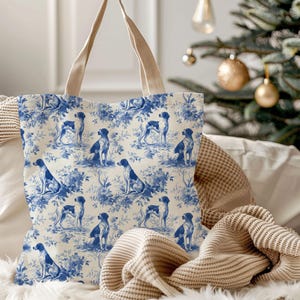 Può includere: Una borsa tote con un motivo ripetitivo in blu e bianco in stile toile raffigurante cani ed elementi floreali. La borsa è dotata di due manici in tessuto beige ed è realizzata in un materiale tessile chiaro con un design stampato.