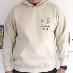 May include: A beige hoodie with a black outline of a dog's head and the text "Custom text" on the front.