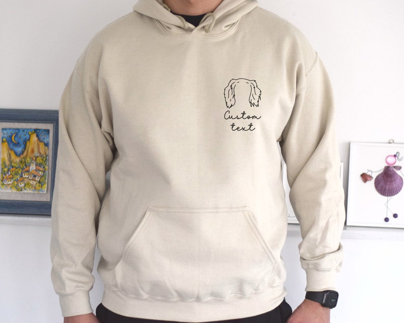 May include: A beige hoodie with a black outline of a dog's head and the text "Custom text" on the front.