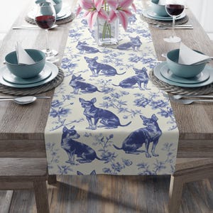 May include: A table runner featuring a repeating pattern of blue chihuahua illustrations and floral motifs on a cream background. The design includes multiple seated dogs in various poses interspersed with detailed botanical elements.