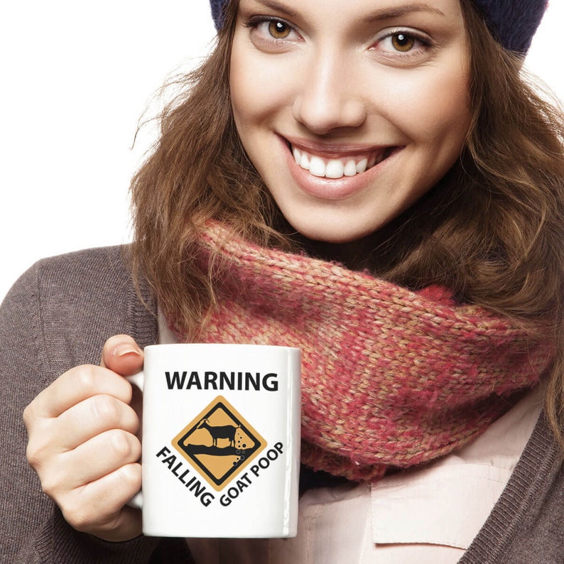 Puede incluir: Taza de cer&aacute;mica blanca con una se&ntilde;al de advertencia negra que dice "WARNING FALLING GOAT POOP". La se&ntilde;al es amarilla con una silueta negra de una cabra y un mont&oacute;n de caca.