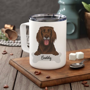 Könnte beinhalten: Weiße Keramik-Reisebecher mit einer braunen Hundefigur und dem Namen "Buddy" auf einem knochenförmigen Grafik.