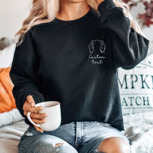 May include: Black sweatshirt with a white outline of a dog's head and the text "Custom text" on the front.
