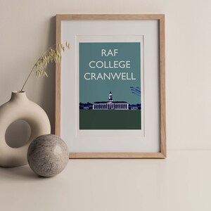 May include: A framed print with a blue and green background featuring a white building with a clock tower and the text "RAF COLLEGE CRANWELL".