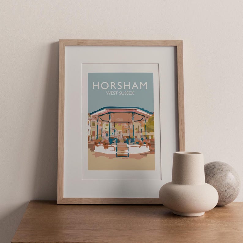 May include: A framed art print depicting the Horsham bandstand in West Sussex. The print features a light blue sky background with the word "Horsham" and "West Sussex" in white text. The bandstand is illustrated in beige, brown, and green.