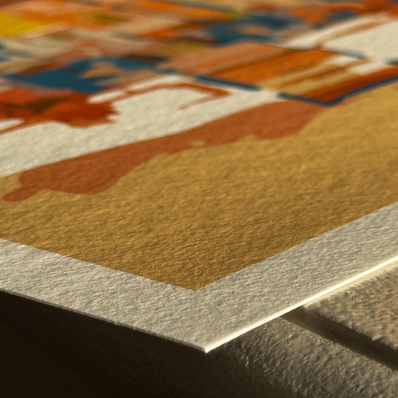 May include: Close-up of a textured paper print with abstract watercolour art. The artwork features a blend of orange, blue, and yellow hues, creating a vibrant and artistic composition. The paper has a rough, tactile surface.
