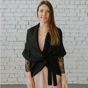 May include: A black knit wrap with lace sleeves. The wrap is tied at the waist and has a relaxed fit.