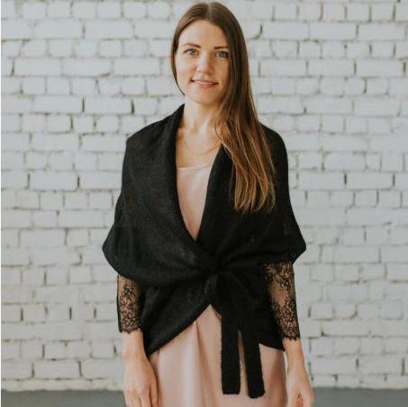 May include: A black knit wrap with lace sleeves. The wrap is tied at the waist and has a relaxed fit.