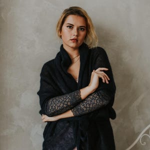 May include: A woman wearing a dark blue knitted cardigan with lace detailing on the sleeves. The cardigan is open in the front and tied at the waist. She is wearing a pink slip dress underneath.