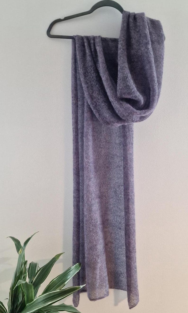 Peut inclure: Une longue &eacute;charpe douce et violette suspendue &agrave; un cintre. L'&eacute;charpe est faite d'un tissu l&eacute;ger et a&eacute;r&eacute; et a une surface l&eacute;g&egrave;rement textur&eacute;e.