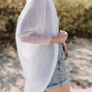 May include: A white knitted cardigan with lace detailing on the sleeves. The cardigan is open at the front and has a relaxed fit.