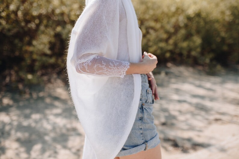 May include: A white knitted cardigan with lace detailing on the sleeves. The cardigan is open at the front and has a relaxed fit.