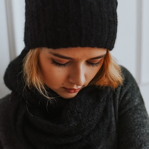 Peut inclure: Une femme portant un bonnet noir en tricot et une &eacute;charpe noire. Elle regarde vers le bas et ses cheveux sont blonds.