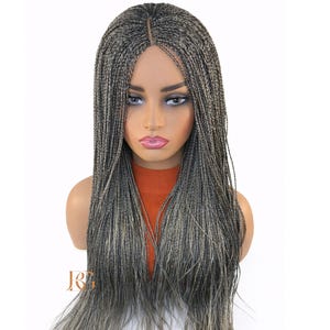 May include: A long, braided wig in shades of grey and blonde is displayed on a mannequin head. The wig features a centre part and long, flowing braids. The mannequin is wearing an orange top, and the background is white.