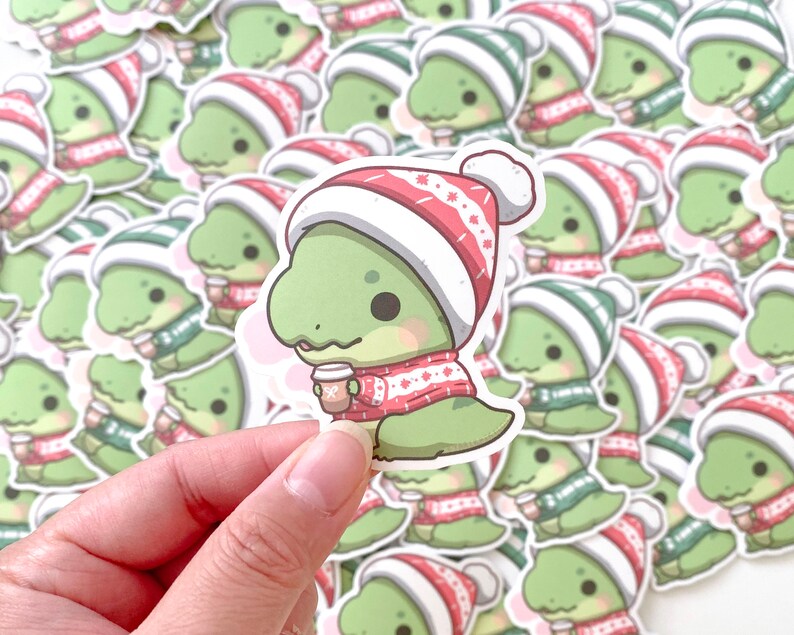 May include: A collection of green dinosaur stickers with red and white winter hats. Each dinosaur is holding a cup of coffee. The stickers are on a white background.