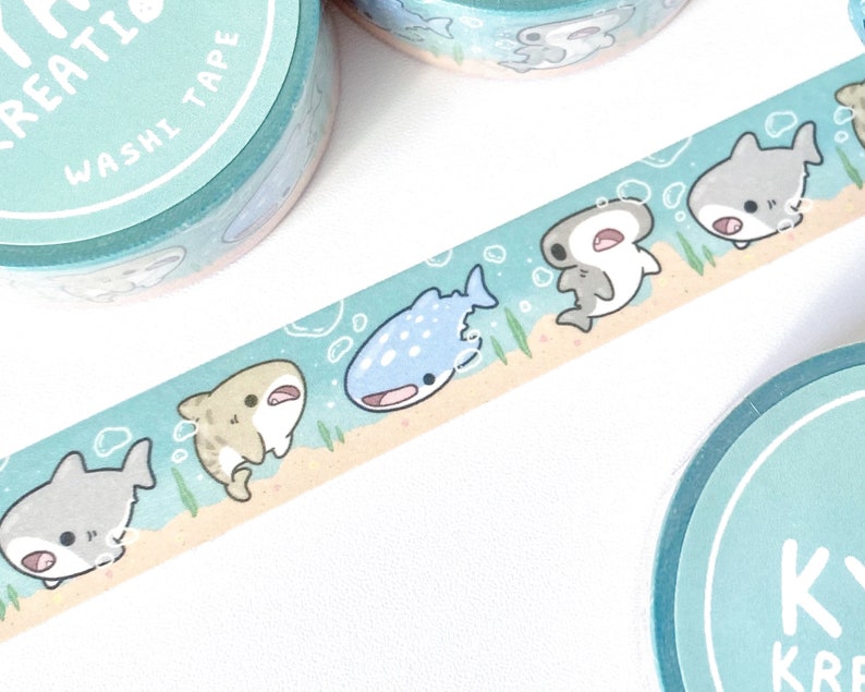 A row of cute shark illustrations printed on a roll of washi tape. Shark species including: hammerheads, great whites, tiger sharks, and whale sharks