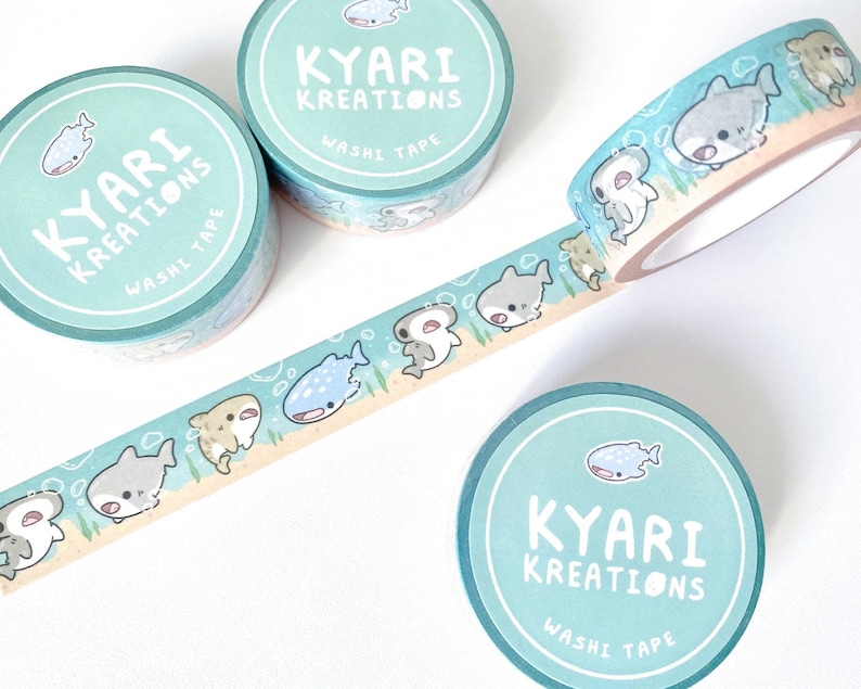 A row of cute shark illustrations printed on a roll of washi tape. Shark species including: hammerheads, great whites, tiger sharks, and whale sharks.  3 additional rolls of washi tapes lying around in background for display purposes