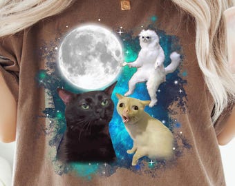 Pode incluir: Uma camiseta marrom com estampa de galáxia com um gato preto, um gato branco e um gato amarelo. A lua é visível no fundo.