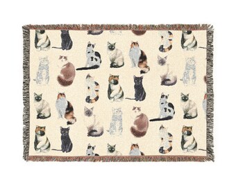 May include: A woven throw blanket featuring a repeating pattern of various cat illustrations in shades of black, brown, gray, and cream. The blanket has a fringed edge and a neutral background.