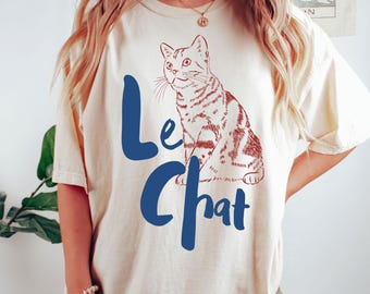 May include: A white t-shirt with a blue and red graphic of a cat and the text "Le Chat".