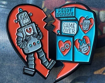 Op de afbeelding: Een rode hartvormige pin met een robot die een gebroken hart vasthoudt en een blauw arcade-spel met de tekst "Robot Romance Game Over".