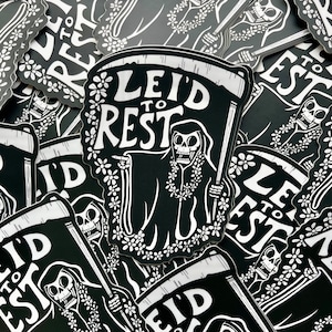 May include: Black and white sticker featuring a Grim Reaper character holding a scythe and a banner that reads "I'd to Rest". The reaper is adorned with a floral lei. The stickers are scattered across a surface.