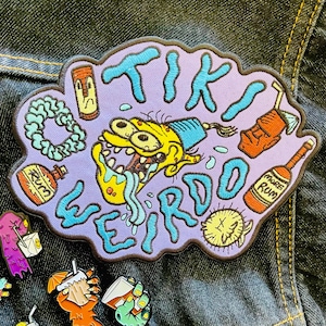 May include: A purple and blue embroidered patch featuring a cartoon character with yellow skin and a blue hat. The character is wearing a lei and has a large mouth with a tongue sticking out. The text "TIKI WEIRDO" is embroidered in blue on the patch.