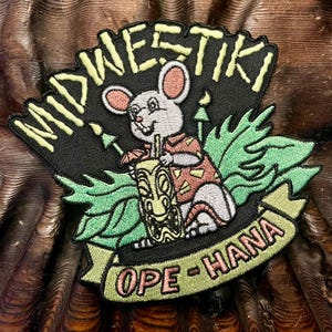 May include: Embroidered patch with the words "MIDWESTIKI" in yellow and a mouse holding a tiki drink. The mouse wears a Hawaiian shirt and is surrounded by green leaves. The banner reads "OPE-HANA".