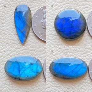 Puede incluir: Cuatro piedras preciosas de labradorita en diferentes formas y tamaños. Las piedras son de un azul profundo con destellos iridiscentes de color. Las piedras se muestran junto a monedas estadounidenses para comparar el tamaño.