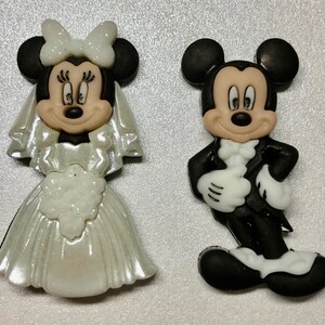 Könnte beinhalten: Ein weißes Brautkleid mit Schleier und ein schwarzer Smoking mit weißer Fliege. Die Figuren sind aus Plastik und stellen Mickey und Minnie Mouse als Brautpaar dar.