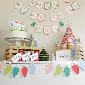 May include: A Christmas-themed first birthday party with a cake decorated with a gingerbread house and the words "It's Christmas! One". The party decorations include a banner that says "Oh What Fun It Is To Be One" and a garland of colorful light bulbs.