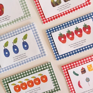 May include: A collection of six rectangular cards featuring illustrations of fruits and food items with holes punched through them. Each card is mounted on a gingham-patterned paper border in various colors, including red, blue, and green.