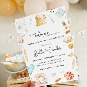 May include: A white invitation card with a watercolor illustration of baking supplies, including a rolling pin, a chef's hat, a bag of flour, a whisk, a measuring cup, a mixing bowl, a pie, a cinnamon stick, and a stand mixer. The text on the card reads "our little cutie pie is turning three! Please join us for a birthday party -celebrating- Betty Crocker Saturday, September 16th, 2024 11:00 am | the smith home 7830 westridge way, birmingham RSVP to Betsy 568.326.4896"
