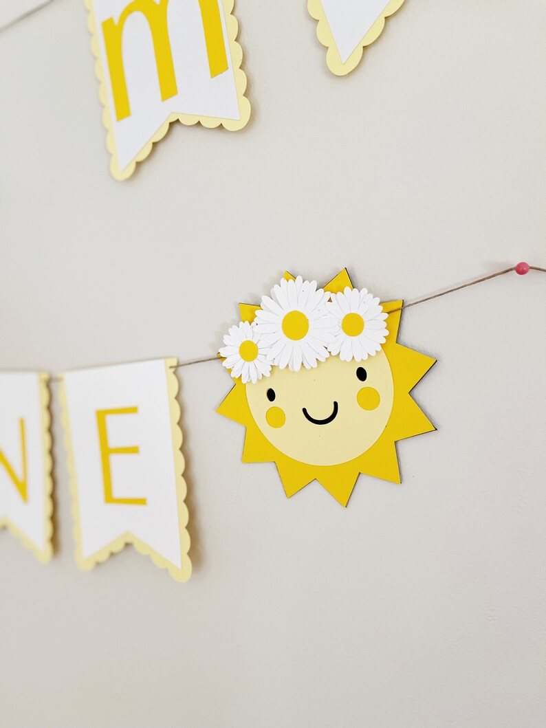 Może przedstawiać: Ż&oacute;łty papierowy baner z napisem "Summer" napisanym białymi literami. Baner jest ozdobiony ż&oacute;łtym słońcem z uśmiechniętą twarzą i białym wiankiem z stokrotek.