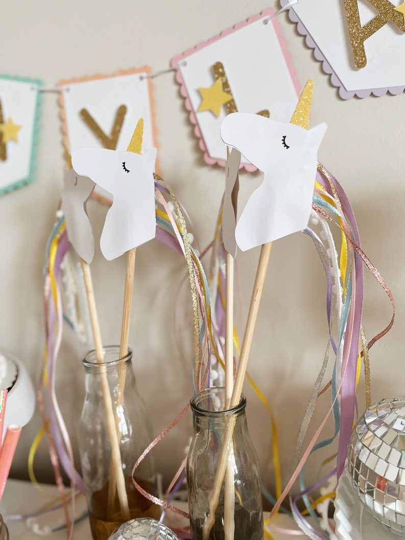 Pu&ograve; includere: Due bacchette a forma di testa di unicorno bianca con nastri arcobaleno e dorati in bottiglie di vetro trasparente. Le teste di unicorno sono di carta e hanno occhi e ciglia neri. Le bacchette sono di legno e sono lunghe circa 30 cm.