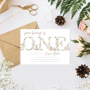May include: A white invitation card with a floral wreath spelling "ONE" with bunnies in the wreath. The text "some bunny is ONE" is at the top of the card. The text "Jessica Rabbit" is below the wreath. The text "HOP ON OVER TO CELEBRATE" is below the name. The date, time, and address are listed below the text. The text "RSVP TO EMILY - CAKE & ICE CREAM WILL BE SERVED" is at the bottom of the card.