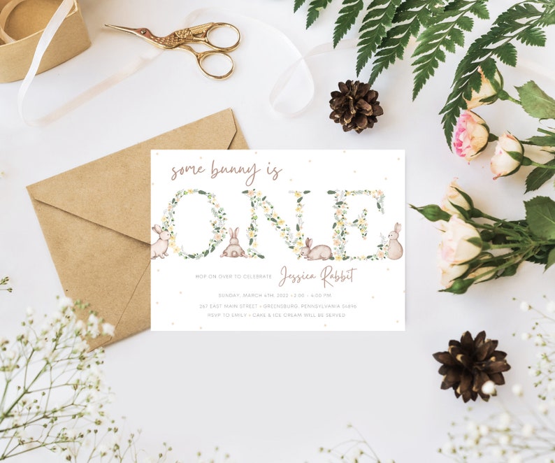 May include: A white invitation card with a floral wreath spelling "ONE" with bunnies in the wreath. The text "some bunny is ONE" is at the top of the card. The text "Jessica Rabbit" is below the wreath. The text "HOP ON OVER TO CELEBRATE" is below the name. The date, time, and address are listed below the text. The text "RSVP TO EMILY - CAKE & ICE CREAM WILL BE SERVED" is at the bottom of the card.
