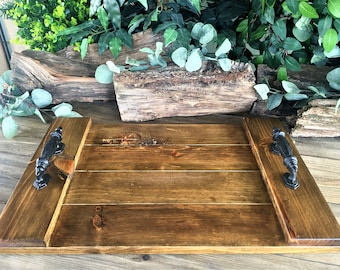 May include: A rectangular wooden serving tray with two black metal handles. The tray is made of natural wood with a dark brown stain. The tray is perfect for serving food or drinks.