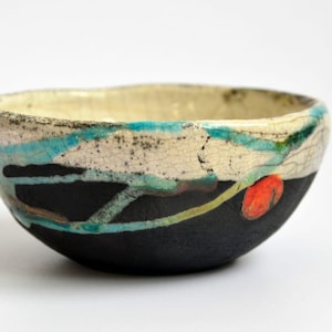 Könnte beinhalten: Eine weiße Keramik-Tasse mit schwarzem Henkel und dem Text "But First, Coffee" in schwarzer, handschriftlicher Schrift. Die Tasse steht auf einer weißen Oberfläche.