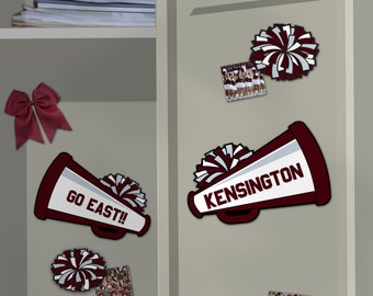 Peut inclure: Deux mégaphones rouges et blancs avec des pompons sur un casier gris. Un mégaphone dit "GO EAST!" et l'autre dit "KENSINGTON".