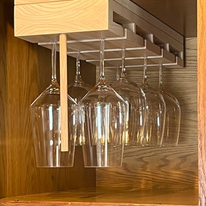 Può includere: Portabicchieri in legno installato all'interno di un mobile. Il portabicchieri è realizzato in legno chiaro e può contenere diversi calici trasparenti. Il mobile è in legno scuro.