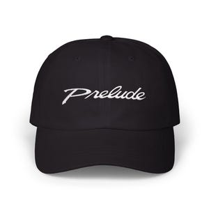 May include: Black baseball cap with the word "Prelude" embroidered in white script across the front. The cap has a curved brim and a structured crown. A classic, casual accessory.