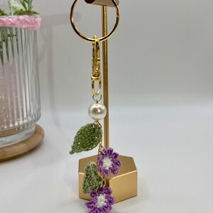 May include: A crocheted flower and leaf keychain with a pearl charm and a gold metal clasp.